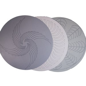 Może przedstawiać: Trzy okrągłe, szare szablony dekoracyjne z różnymi wzorami geometrycznymi. Górny szablon ma wirujący wzór spiralny. Środkowy szablon ma powtarzający się, zakrzywiony wzór linii. Dolny szablon ma powtarzający się, zakrzywiony wzór liści.