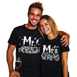 May include: A couple wearing matching black t-shirts with white text. The man's shirt says "Mr. We're up to no good" with a lightning bolt and a banner. The woman's shirt says "Mrs. We solemnly swear" with a lightning bolt and a banner.