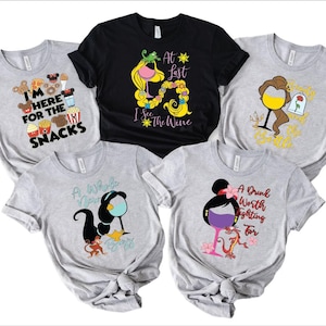 May include: Five different t-shirts featuring various Disney princess-themed designs. The shirts are all grey or black with colourful graphics. The designs include a princess with a glass of wine, a princess with a glass of wine and a rose, a princess with a glass of wine and a monkey, a princess with a glass of wine and a dragon, and a princess with a glass of wine and a crown. The text on the shirts includes "I'm here for the snacks", "At last I see the wine", "A whole new world", "A drink worth fighting for", and "Beauty and the Bottle".