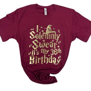 May include: Burgundy t-shirt with a gold glitter design that says "I solemnly swear it's my 36th birthday".