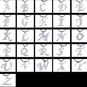 Puede incluir: Un conjunto de 26 colgantes de plata, cada uno con una letra diferente del alfabeto adornada con diamantes de imitación transparentes. Los colgantes están en cordones negros.