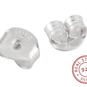 Puede incluir: Dos respaldos de pendientes de plata, uno con un sello 925, y un círculo rojo con el texto "REAL STERLING 925 SILVER".