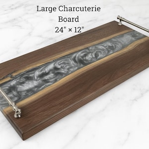 May include: Large charcuterie board, 24" x 12", made of dark wood with a silver resin river design. Features metal handles on each end. Ideal for serving appetizers and cheeses.