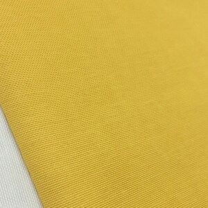 Può includere: Primo piano di un tessuto giallo con trama testurizzata. Il tessuto ha una leggera lucentezza e una superficie liscia e uniforme.
