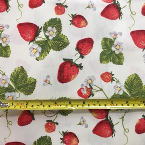 May include: White fabric with a repeating pattern of red strawberries and green leaves. A yellow measuring tape is placed across the fabric, showing measurements in inches.