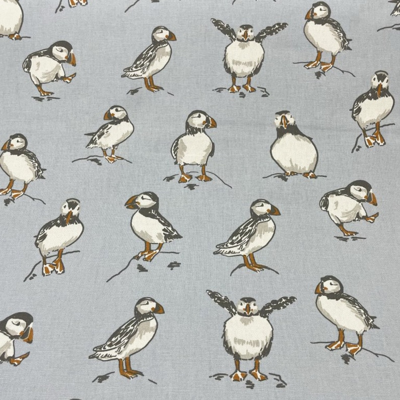 Peut inclure: Un tissu bleu et blanc avec un motif r&eacute;p&eacute;titif de macareux. Les macareux sont dans diff&eacute;rentes poses, certains avec les ailes d&eacute;ploy&eacute;es, certains avec le bec ouvert et certains avec la t&ecirc;te inclin&eacute;e. Le tissu est de couleur bleu clair avec un fond blanc.