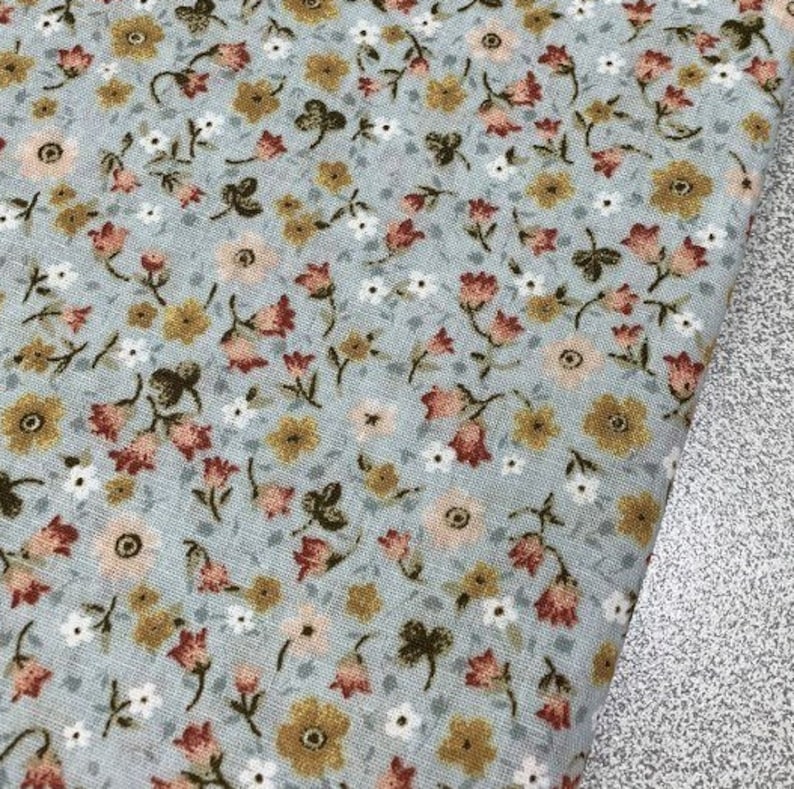 May include: A light blue fabric with a small floral pattern. The flowers are in shades of pink, yellow, and brown.