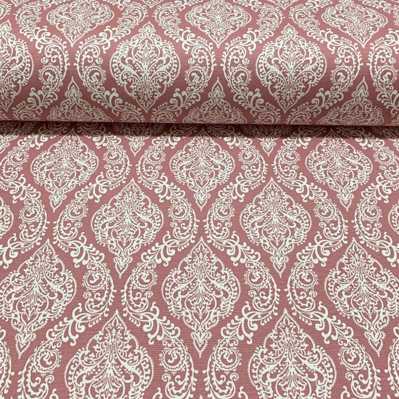 May include: Pink fabric with a white damask pattern. The pattern features intricate floral designs and swirls.