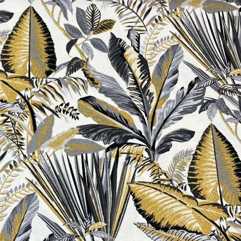 May include: A fabric with a tropical leaf pattern. The design features large leaves in shades of gold, grey, and black against a white background. The leaves are arranged in a dense, overlapping pattern, creating a lush, jungle-like effect.