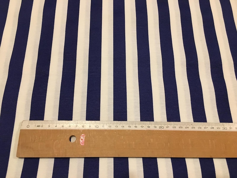 Op de afbeelding: Witte stof met blauwe strepen. Een liniaal ligt op de stof om de breedte van de strepen te laten zien. De liniaal is 76 cm lang.