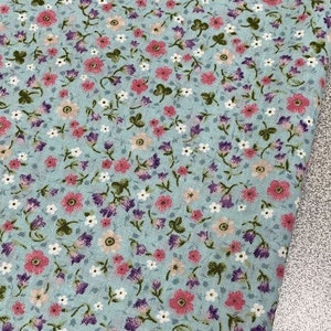 May include: A light blue fabric with a small floral pattern. The pattern features pink, white, and purple flowers on a light blue background.