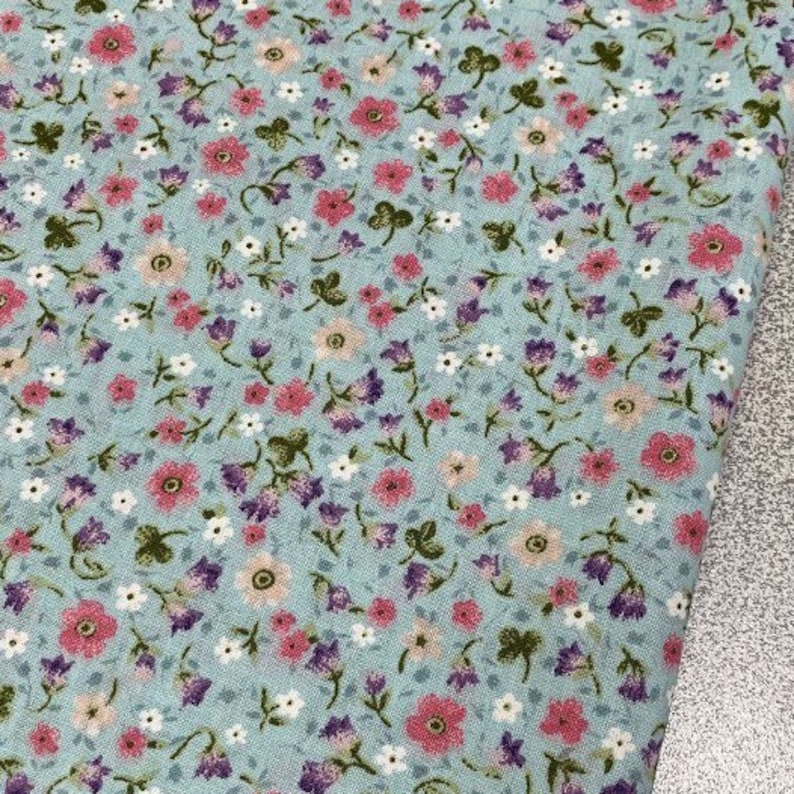 May include: A light blue fabric with a small floral pattern. The pattern features pink, white, and purple flowers on a light blue background.
