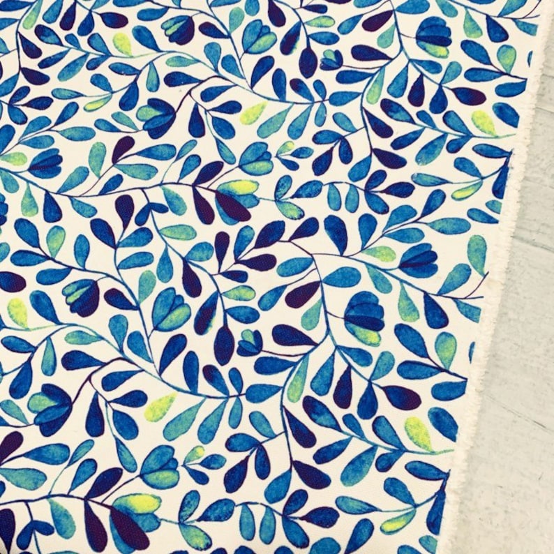 Op de afbeelding: Witte stof met een blauw en groen bloemenpatroon. Het patroon bevat kleine bladeren en bloemen in tinten blauw en groen.