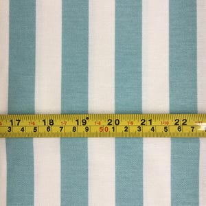 May include: A close-up of white and teal striped fabric with a yellow measuring tape across the bottom. The tape reads "17 18 19 20 21 22".