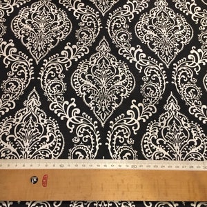 May include: Black fabric with a white damask pattern. The fabric is measured with a ruler.