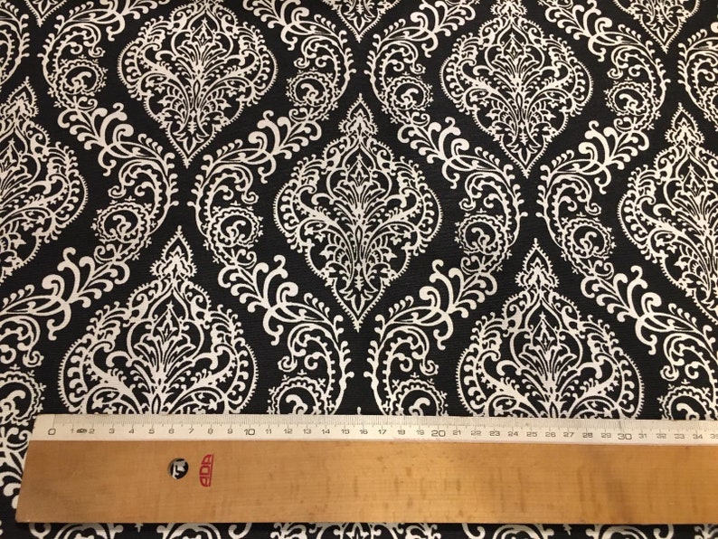 May include: Black fabric with a white damask pattern. The fabric is measured with a ruler.