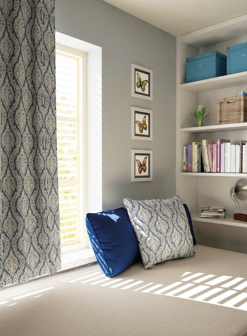 May include: A window seat with a blue and white patterned curtain, two pillows, and a bookshelf with books and decorative items. The wall is painted a light gray color and there are three framed pictures of butterflies.
