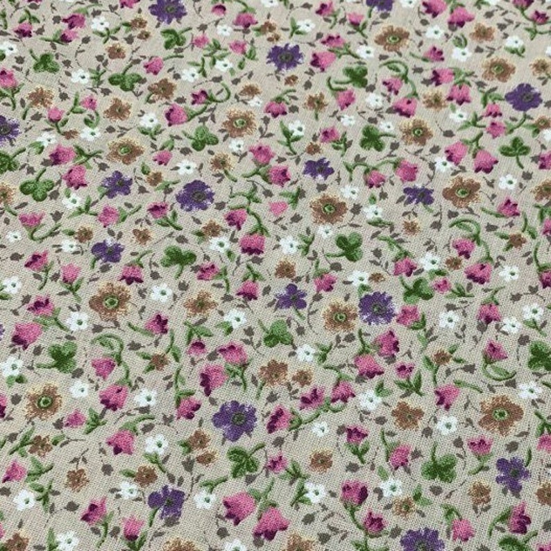 May include: A beige fabric with a small-scale floral print. The print features pink, purple, and brown flowers on a beige background.