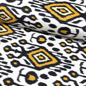 May include: White fabric with a repeating pattern of black and yellow geometric shapes. The design includes diamond and oval shapes, creating a bold, abstract print. The fabric is folded, showing the texture and drape of the material.
