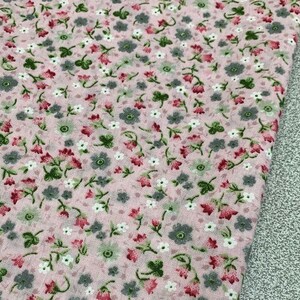 May include: Pink fabric with a small floral print. The fabric features a repeating pattern of tiny pink, white, and gray flowers.