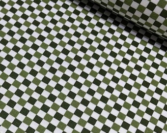 May include: Close-up of a fabric with a checkered pattern. The design features a repeating grid of squares in white, olive green, and dark green. The fabric is folded over in the upper right corner, showing the texture and drape of the material.