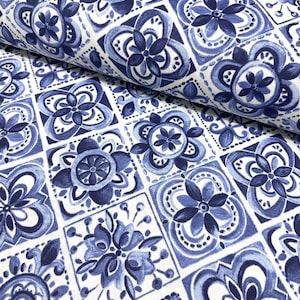 May include: White fabric with a repeating pattern of blue floral designs. The pattern features stylized flowers and geometric shapes in shades of blue, creating a decorative and artistic look. The fabric is likely suitable for various craft and sewing projects.