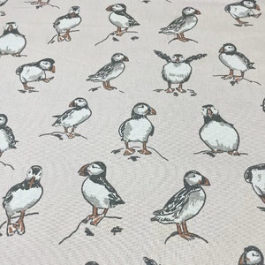 Peut inclure: Un tissu beige avec un motif r&eacute;p&eacute;titif de macareux noirs et blancs. Les macareux sont dans diverses poses, y compris debout, en vol et en train de nager.