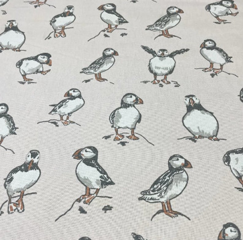 Peut inclure: Un tissu beige avec un motif r&eacute;p&eacute;titif de macareux noirs et blancs. Les macareux sont dans diverses poses, y compris debout, en vol et en train de nager.