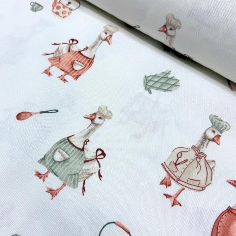 May include: White fabric with a repeating pattern of geese wearing chef hats and aprons. The geese are holding kitchen utensils and there are other kitchen-themed illustrations like a pot and a spoon.