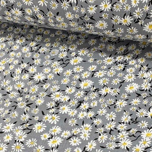 May include: Grey fabric with a white daisy print. The daisies have yellow centres.