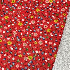 May include: Red fabric with a small floral print. The print features blue, yellow, pink, and green flowers on a red background.