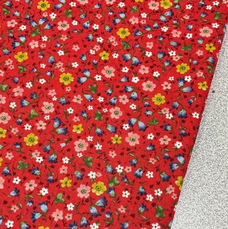 May include: Red fabric with a small floral print. The print features blue, yellow, pink, and green flowers on a red background.