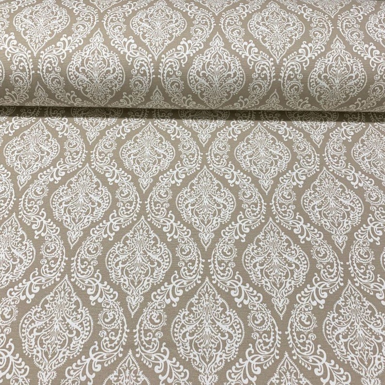 May include: Beige fabric with a white damask pattern. The pattern features intricate floral designs and swirls.