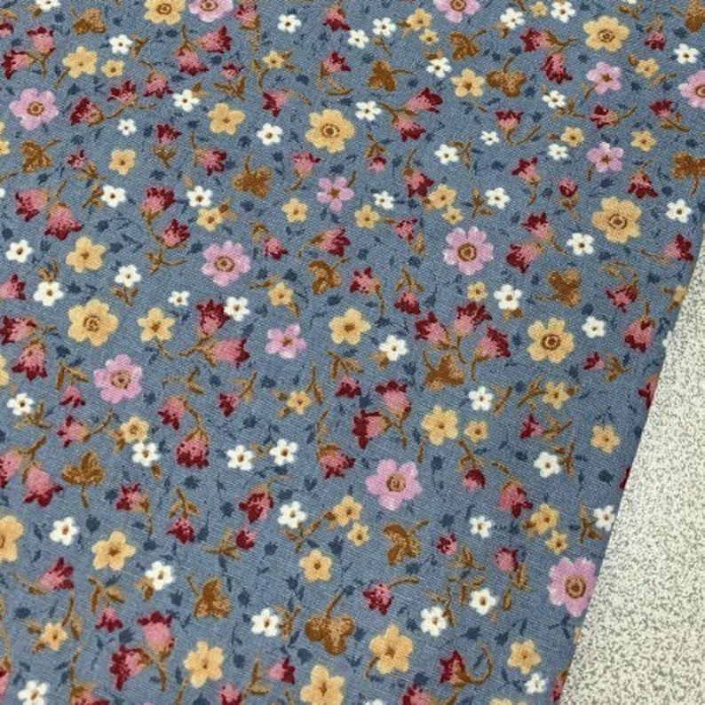 May include: A blue fabric with a small floral print in shades of pink, white, and brown. The fabric is perfect for crafting projects, quilting, and home decor.