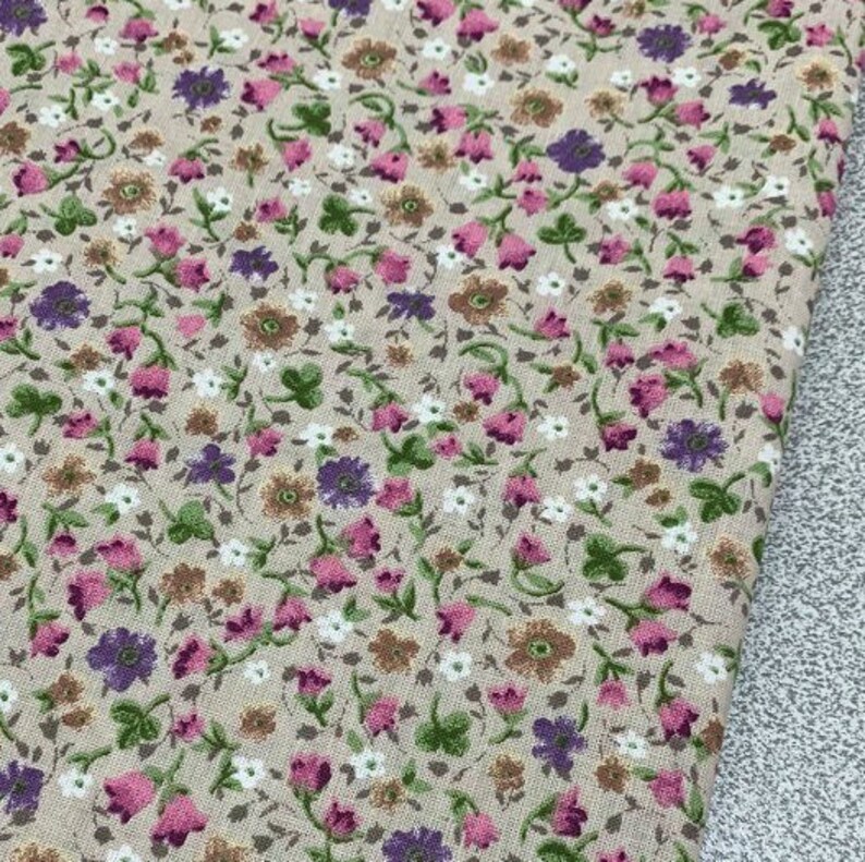 May include: Beige fabric with a small-scale floral print featuring pink, purple, and brown flowers. The fabric has a subtle texture.