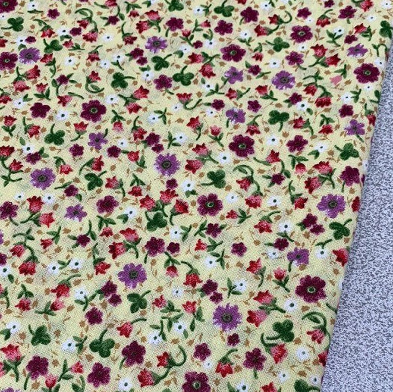 May include: A yellow fabric with a small floral print. The flowers are purple, red, and white.