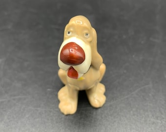 Peut inclure: Une petite figurine en céramique d'un chien brun et blanc avec un nez rouge. Le chien est assis, la tête inclinée sur le côté.