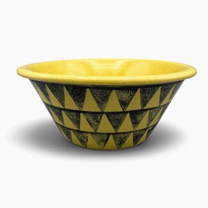 May include: A yellow bowl with a speckled finish and a wide, rounded rim. The exterior features two horizontal bands of repeating black triangles arranged in a geometric pattern, creating a stark contrast against the bright yellow base color.