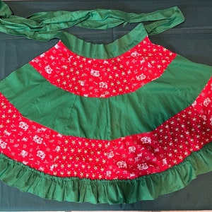 May include: A red and green skirt with a white print of small animals. The skirt has a green ruffle around the bottom and a green sash.