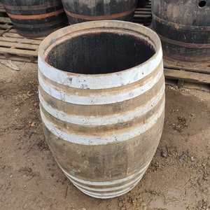 May include: A used wooden barrel with white painted hoops. The interior is dark, and the exterior shows signs of wear. Other barrels are visible in the background, suggesting a rustic or vintage theme.