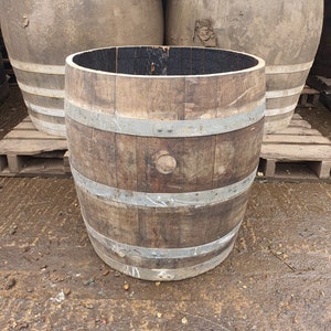 May include: A rustic, open-top wooden barrel with metal hoops, showing signs of age. The barrel is a natural brown colour with a dark interior. Two other barrels are in the background.