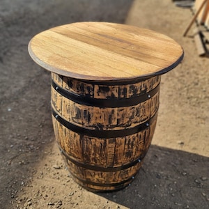 Op de afbeelding: Een houten vaten tafel met een rond blad en zwarte metalen banden. De tafel is gemaakt van gerecycled hout en heeft een rustieke uitstraling.
