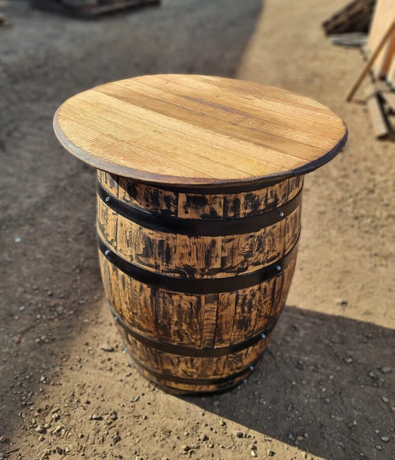 Op de afbeelding: Een houten vaten tafel met een rond blad en zwarte metalen banden. De tafel is gemaakt van gerecycled hout en heeft een rustieke uitstraling.