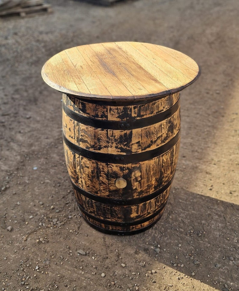 Op de afbeelding: Een houten vaten tafel met een zwarte gebeitst afwerking en een natuurlijk houten blad. Het vat is gemaakt van eikenhout en heeft metalen banden.