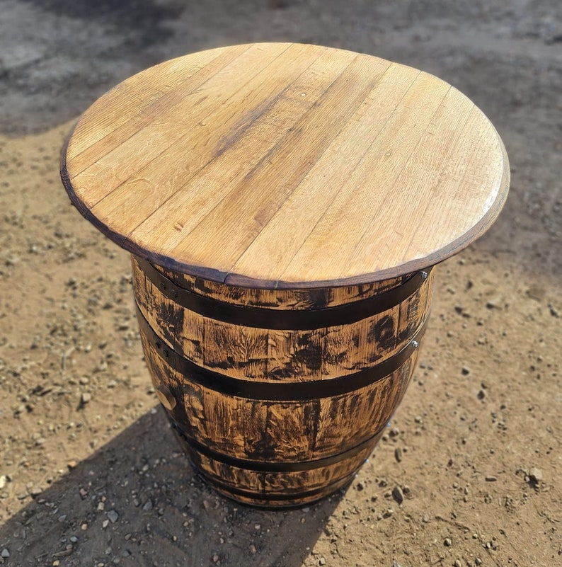 Op de afbeelding: Een houten vaten tafel met een naturel houten blad en zwarte metalen banden. De tafel is gemaakt van gerecycled hout en heeft een rustieke uitstraling.