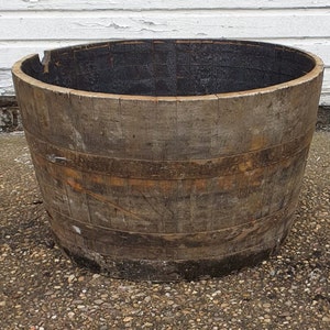 May include: A large, wooden barrel planter with a natural brown finish. The barrel is made of wood staves and has metal hoops around it. The barrel is empty and ready to be planted with flowers or other plants.