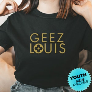 May include: Black t-shirt with a gold graphic that says "GEEZ LOUIS" with a stylized flower logo. Youth sizes available.