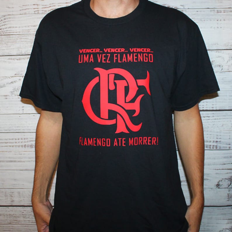 Puede incluir: Camiseta negra con un gr&aacute;fico rojo del logotipo del equipo de f&uacute;tbol Flamengo. El texto "VENCER. VENCER. VENCER... UMA VEZ FLAMENGO" y "FLAMENGO ATE MORRER!" est&aacute; impreso en la camiseta.
