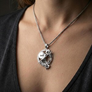 Polished silver Athena warrior pendant necklace worn on the neck, clean lifestyle wear shot capturing bright shine and the detailed spear-and-shield relief in natural light.