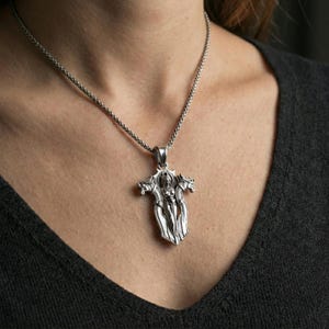 Polished silver gothic cross pendant necklace worn on the neck, clean lifestyle wear shot capturing bright shine and the intricate angel relief in motion.